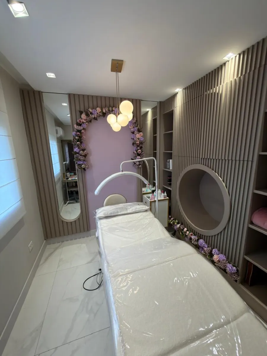 Sala de procedimentos da Lizviê Clinic com maca, arco de flores lilás e painel ripado